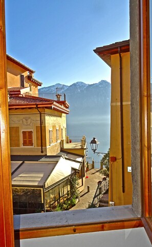 Vista desde una ventana que da a un paisaje montañoso, con arquitectura tradicional que incluye balcones e igualmente una farola.