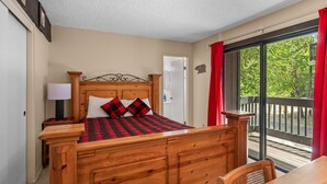 Une chambre à coucher avec un lit en bois, une table de chevet, une lampe et une vue sur l’extérieur grâce à une porte-fenêtre coulissante.