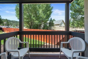 En overdækket udendørs terrasse med to hvide plastikstole, et trædæk og udsigt til et boligområde med huse og træer.