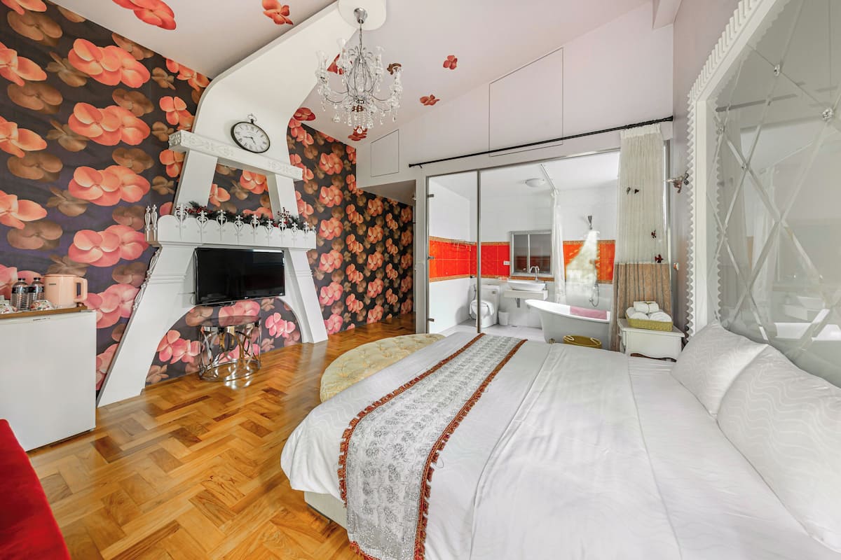 Un dormitorio con una cama grande, televisor, chimenea y baño visible a través de una puerta de vidrio.