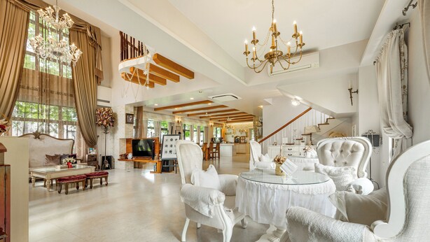 A spacious living room with a high ceiling, chandeliers, and a staircase leading to an upper level. - Pass Happiness On (Wujie)