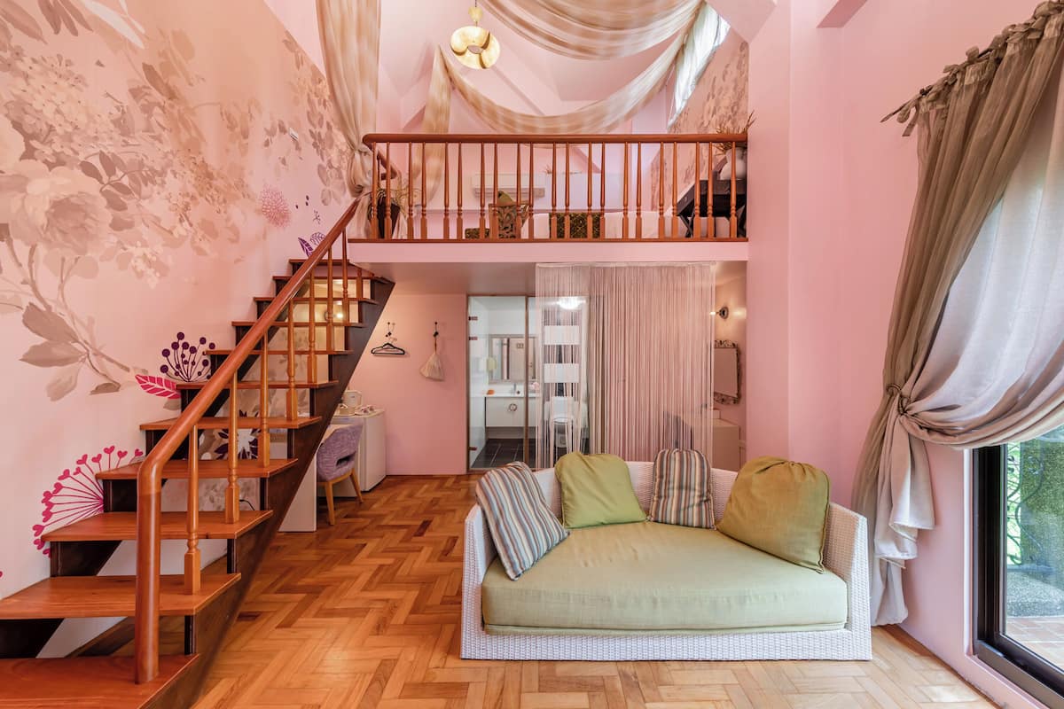 Una sala de estar acogedora con piso de espiga, una escalera de madera, un sofá con cojines y vistas a través de una ventana.