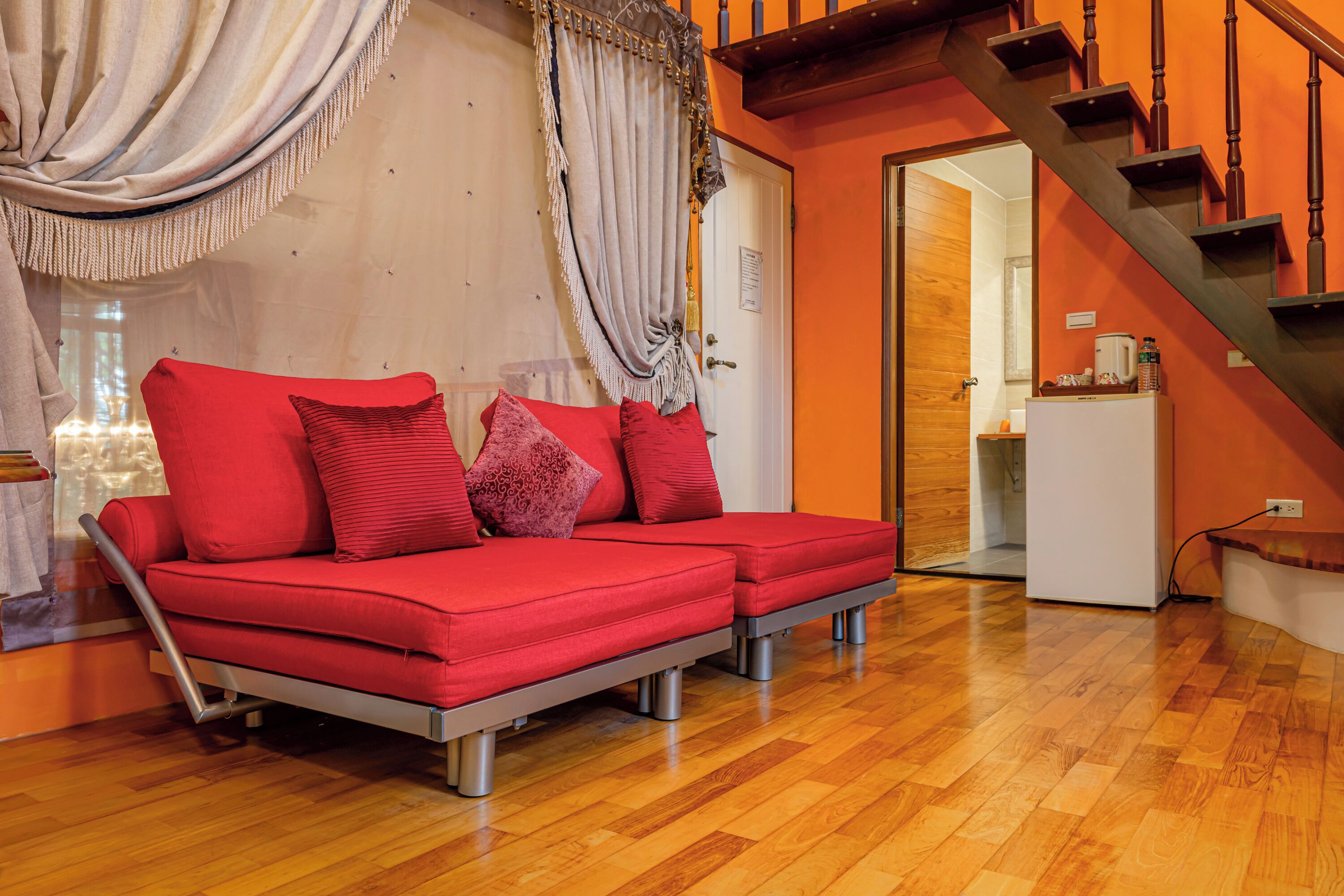 A modern living room with a red sofa, wooden flooring, and a staircase.