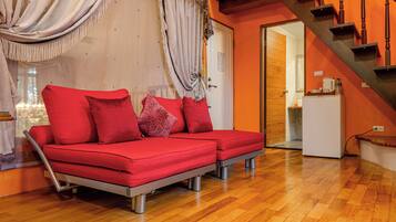 A modern living room with a red sofa, wooden flooring, and a staircase.