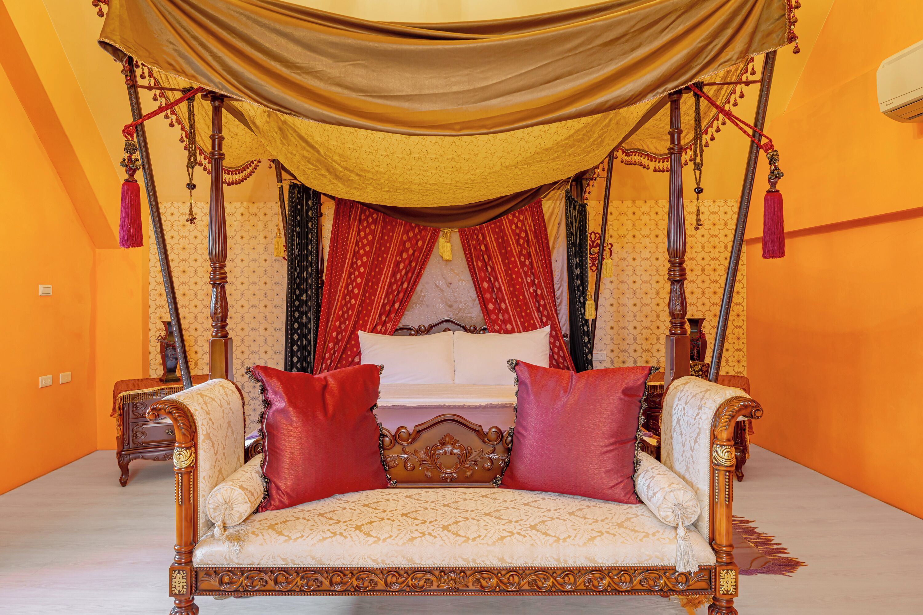 Una cama lujosa con dosel, muebles de madera ornamentados y almohadas rojas.