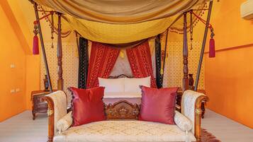 Una cama lujosa con dosel, muebles de madera ornamentados y almohadas rojas.