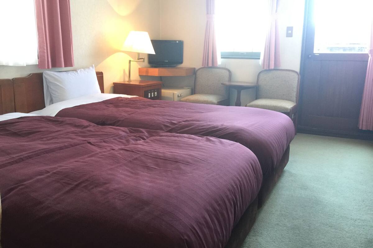 A hotel room with two beds, a TV, a lamp, a chair, and a small table.