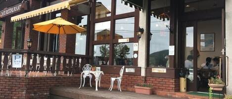 Una cafetería con terraza, un toldo verde y fachada de ladrillo.