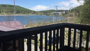 A view from a balcony overlooking a lake with a forested hillside in the background.