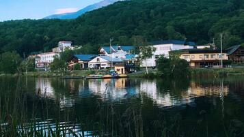 A lakeside town with buildings along the shore, a mountain in the background, and a calm water surface reflecting the structures.