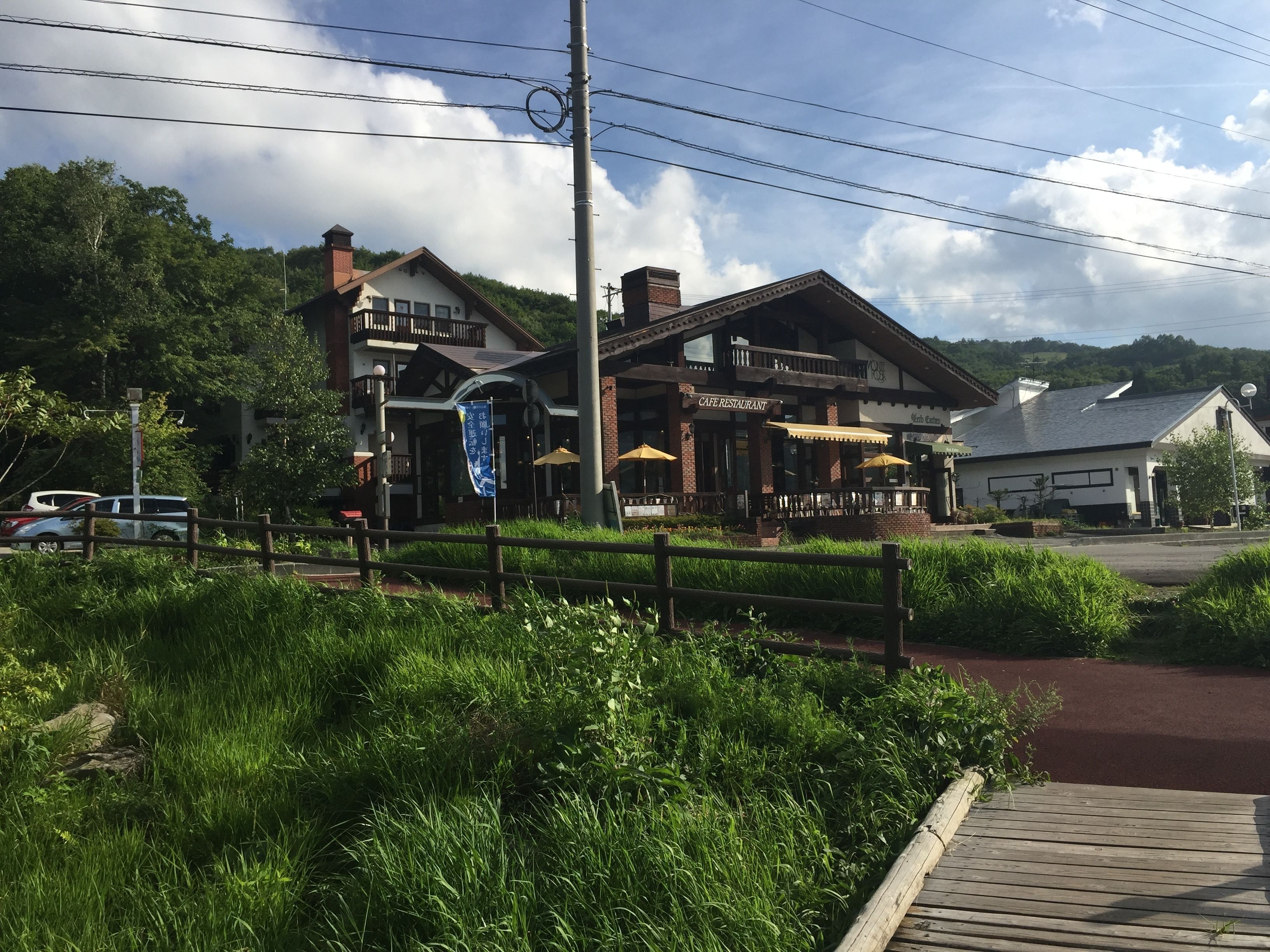 A cafe restaurant with outdoor seating, surrounded by greenery and a wooden fence.