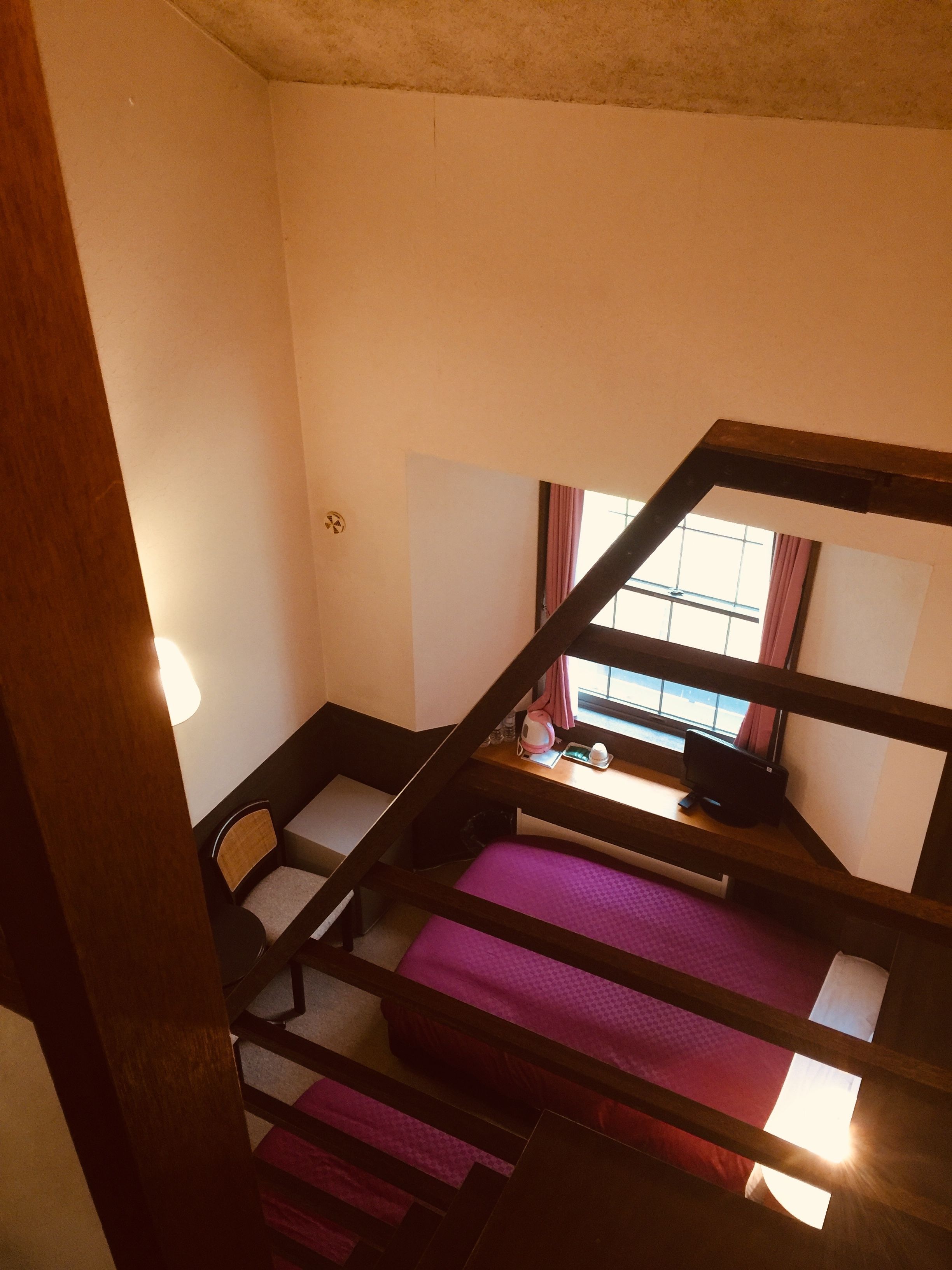 A dormitory room with bunk beds, a desk, a chair, and a window with curtains.