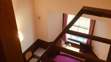 A dormitory room with bunk beds, a desk, a chair, and a window with curtains.