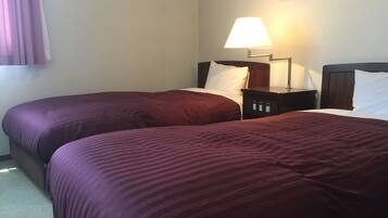 A hotel room with two beds, each with a dark-colored bedspread, a bedside table with a lamp, and a wall-mounted picture frame.