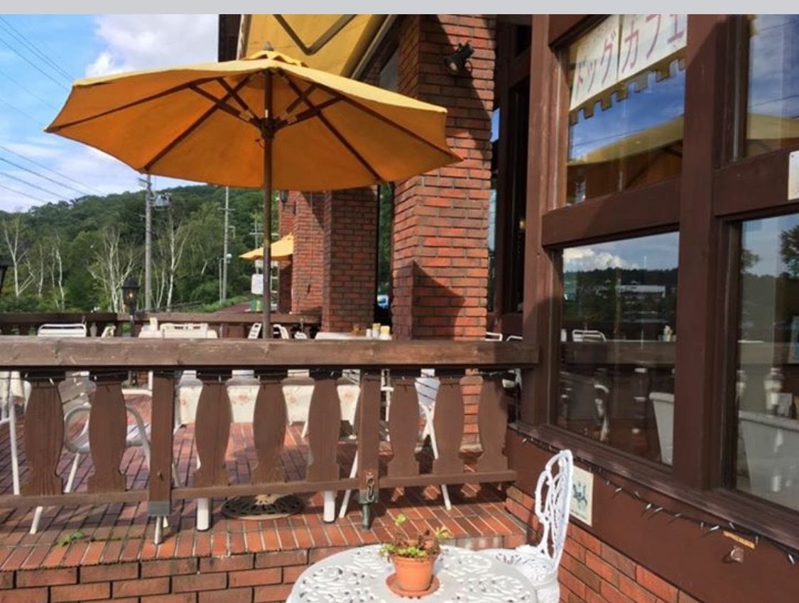 An outdoor seating area with a brick wall, a yellow umbrella, and a white chair.