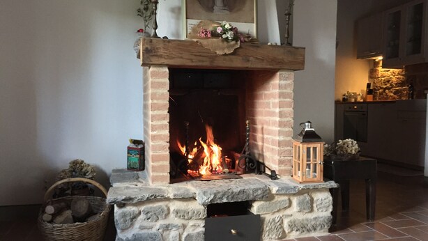 Une cheminée en pierre avec un feu de bois, un panier de bûches et une petite table sur laquelle est posée une lanterne.