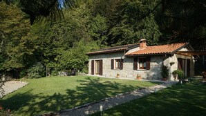 Une maison en pierre avec un toit en tuiles, entourée d’une pelouse bien entretenue et d’arbres.