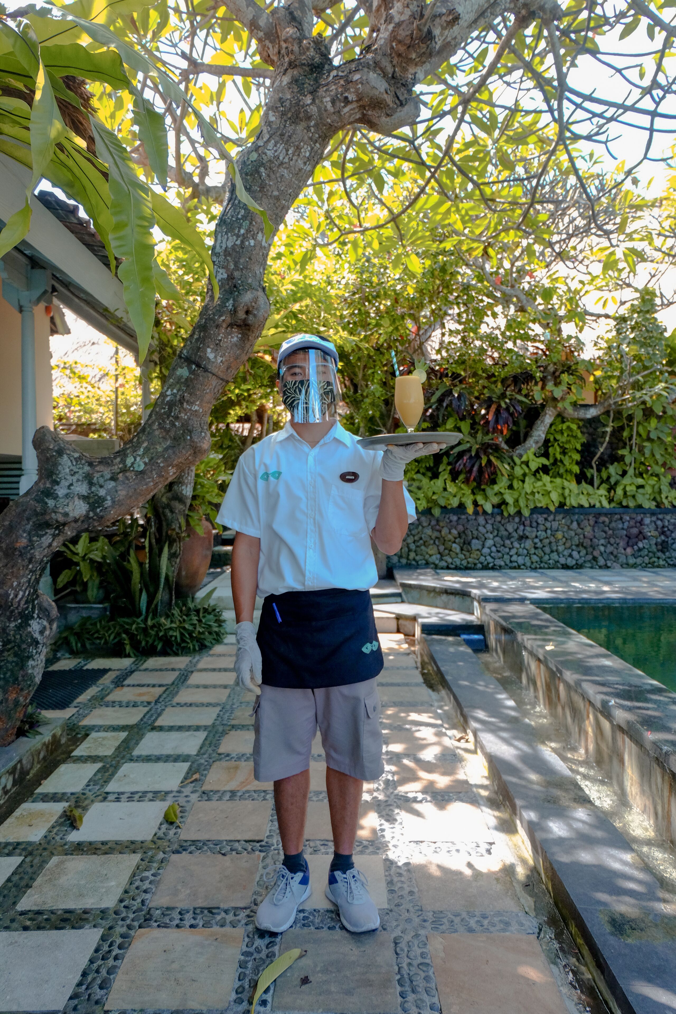 A person standing in a garden area with a pool and a stone pathway.