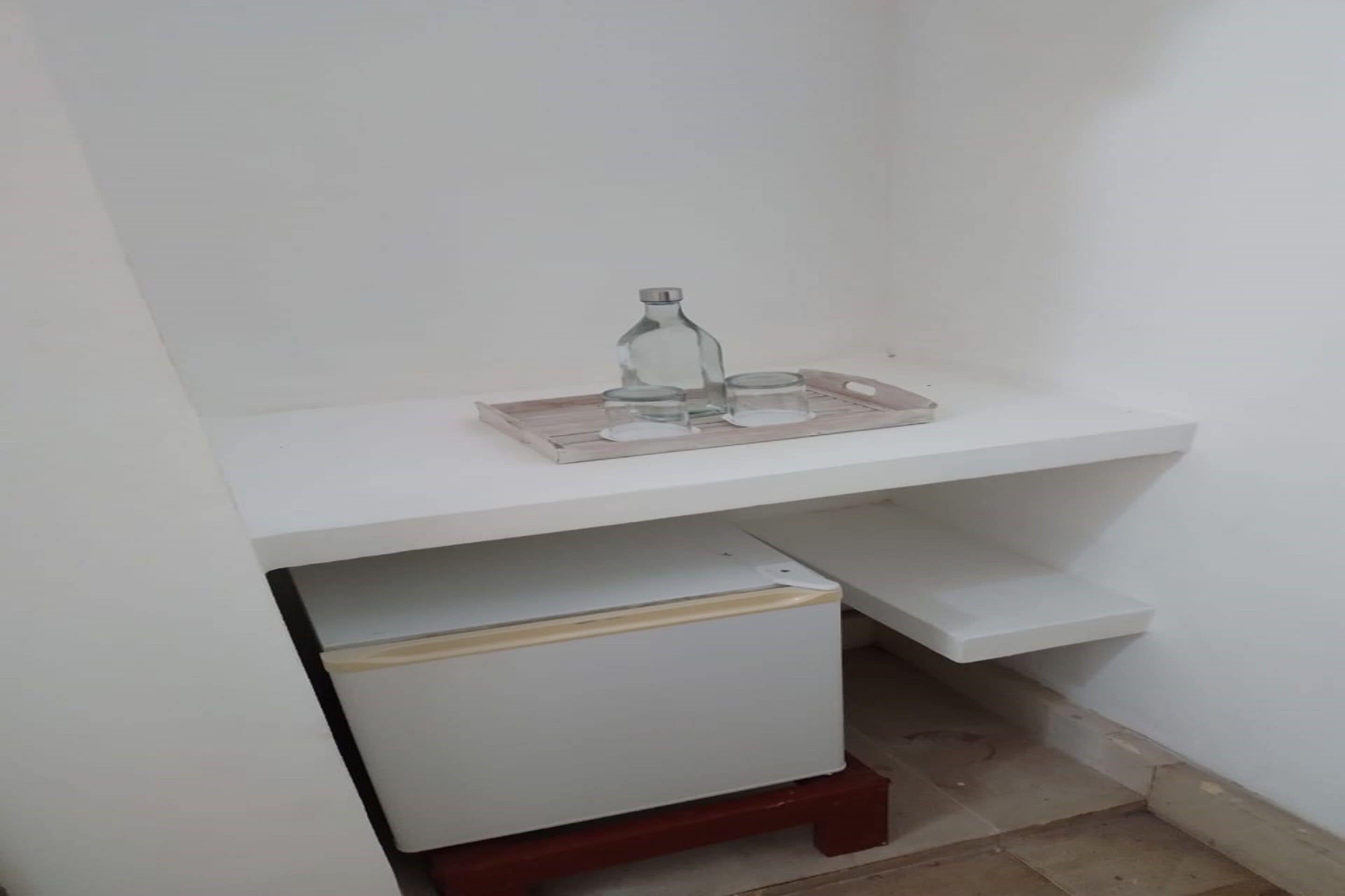Una estantería blanca con una botella de vidrio y dos vasos sobre una bandeja.