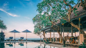 A serene pool area with lounge chairs and umbrellas, surrounded by lush greenery and overlooking the ocean. - Alam Candi Resort (Karangasem)