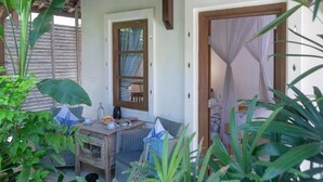 A cozy outdoor seating area with a wicker table and chairs, surrounded by lush greenery. - Alam Candi Resort (Karangasem)