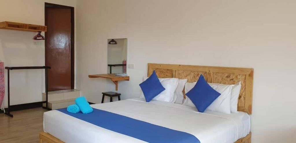 A neatly made bed with blue and white bedding, a wooden headboard, and a small bedside table with a mirror.