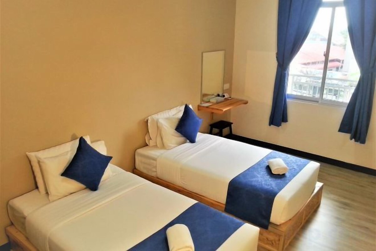 A hotel room with two beds, a small table, a mirror, and a window with curtains.