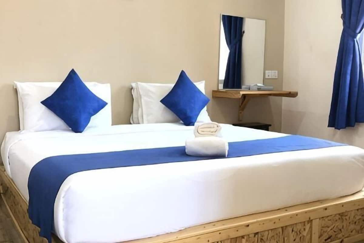 Un letto con biancheria da letto bianco e blu, una testiera in legno, un comodino di legno con uno specchio e tende blu.