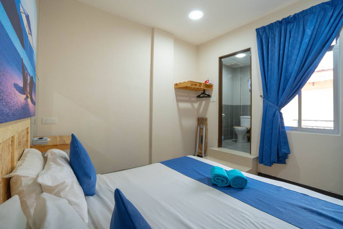 Camera d'albergo con un letto, una testiera in legno, un asciugamano blu e una finestra con tende blu.