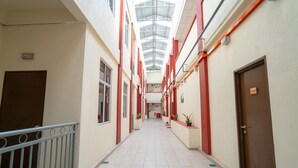 Un pasillo con techo alto, elementos estructurales rojos y plantas en macetas a lo largo de las paredes.
