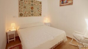 Ein Schlafzimmer mit einem großen Bett, zwei Nachttischen mit Lampen, einem Schaukelstuhl, einer gemusterten Wandteppich und einem Gemälde an der Wand.