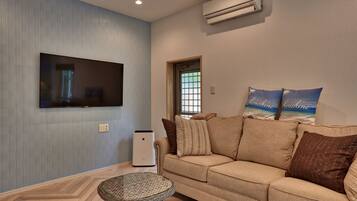 A living room with a beige sofa, a flat-screen TV mounted on the wall, and a small round table.