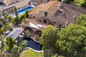 Vue aérienne d’un bâtiment en pierre doté d’une piscine, d’un patio couvert et d’un petit pont.