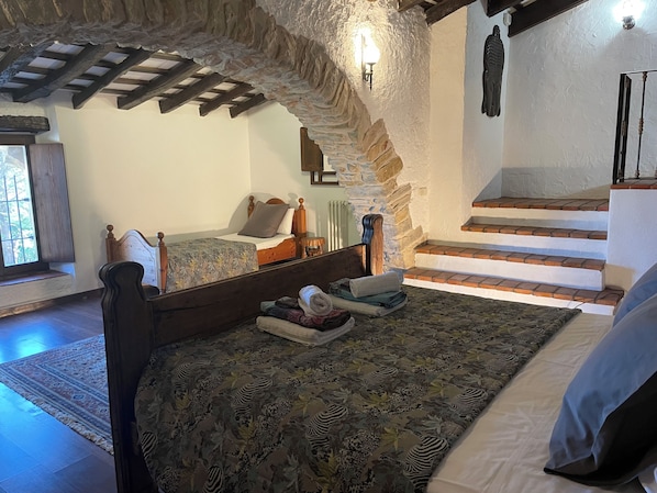 Une chambre avec un lit en bois, un mur en pierre et un escalier.