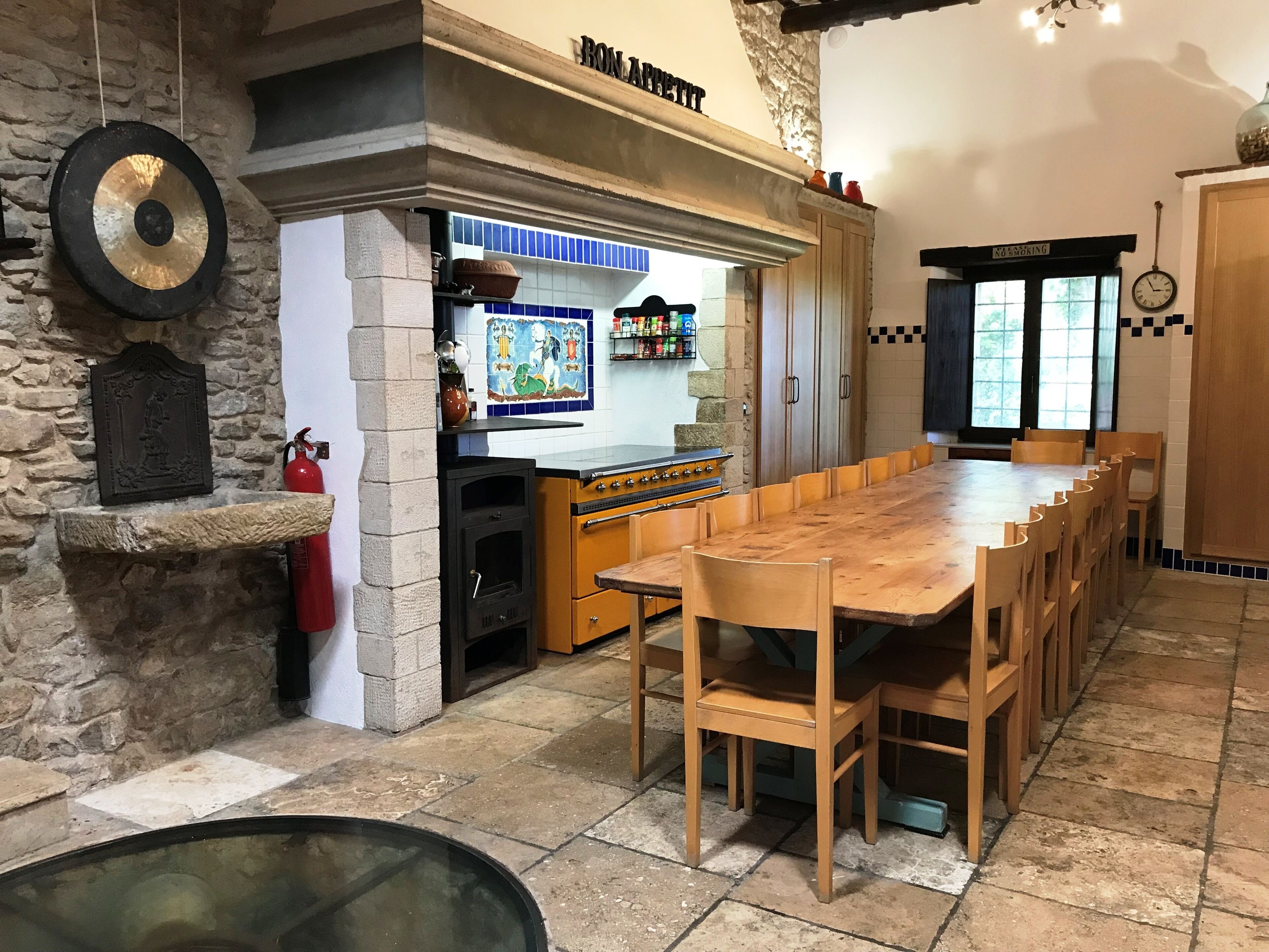 A rustic kitchen with a stone wall, a wooden table, and a tiled backsplash.
