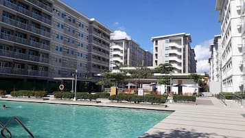 A modern hotel with a swimming pool, multiple balconies, and a clear sky.