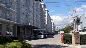 Un hôtel à plusieurs étages doté de balcons, d’une entrée couverte et d’un parking où sont garées des voitures.