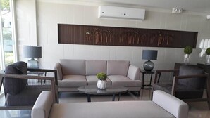 Un salon moderne avec un canapé, des fauteuils et une table basse. Un élément décoratif orne le mur au-dessus du canapé, et une petite plante est posée sur la table basse.