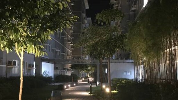 Un chemin piétonnier éclairé, traversant un quartier résidentiel bordé d’arbres et de bâtiments illuminés.