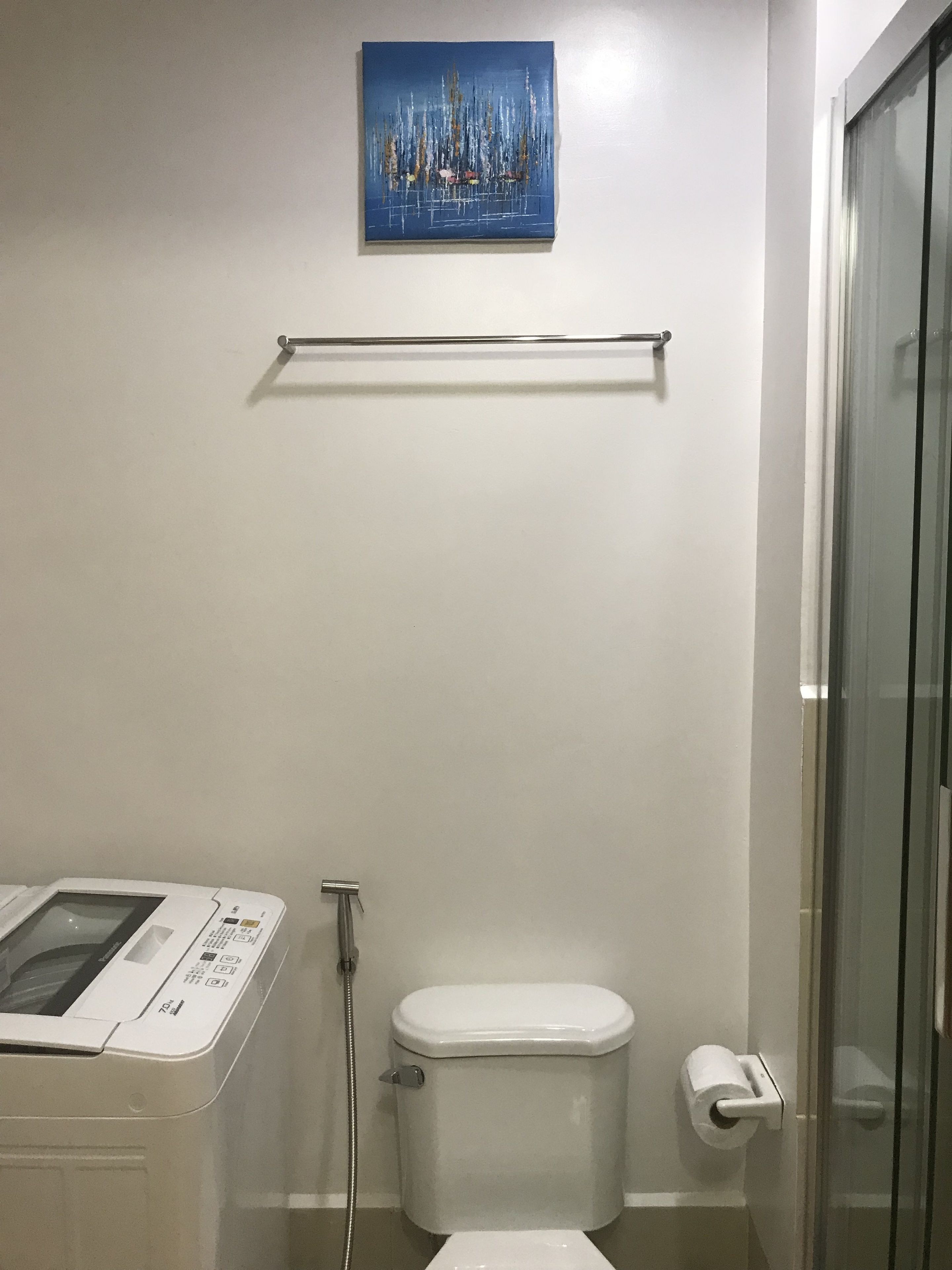 Une salle de bain équipée d’un lave-linge, de toilettes et d’une douche à parois de verre.