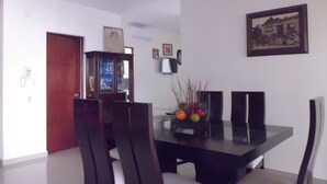 Un coin repas avec une table en bois foncé, des chaises blanches et un centre de table composé de fruits.