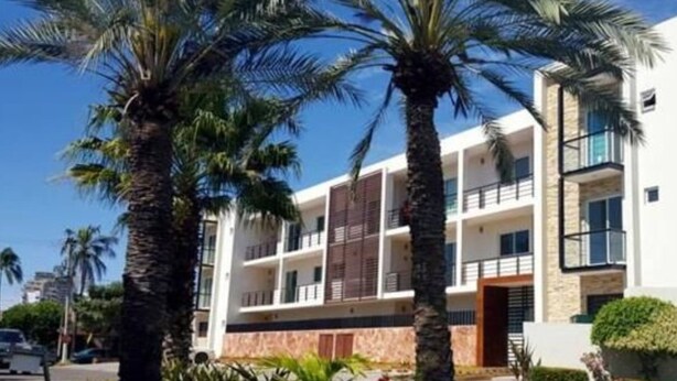 Un hôtel moderne à plusieurs étages, doté d’une cour intérieure, de palmiers et surplombant un ciel d’un bleu éclatant.