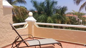 A sun lounger on a tiled terrace with a view of palm trees and buildings. - Condo P Iguana (Mazatlán)