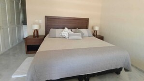 A bedroom with a large bed, two bedside tables with lamps, a wooden headboard, and a view of a corridor with doors. - Condo P Iguana (Mazatlán)