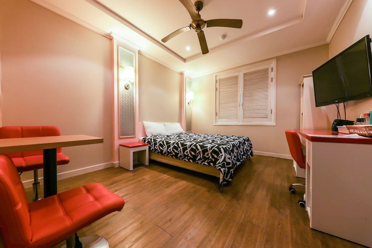 Un dormitorio con cama, escritorio, silla, ventilador de techo y televisor.