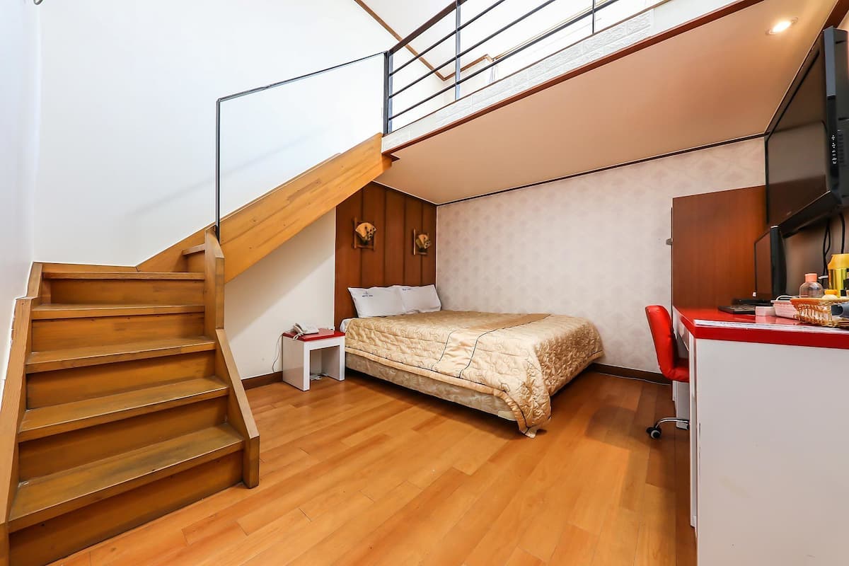 Un dormitorio con escalera de madera, cama, escritorio y televisor.