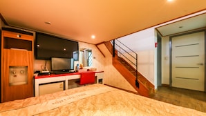 A hotel room with a bed, a desk with a computer, a television, and a staircase leading to another room. - Blue Motel (Boryeong)