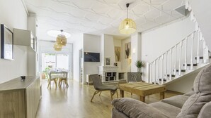 Een moderne woonkamer met houten vloer, een grijze bank, een houten salontafel en een trap met witte leuningen.