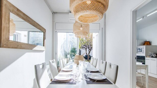 Een moderne eetruimte met een lange tafel voor zes personen, witte wanden en een groot raam.