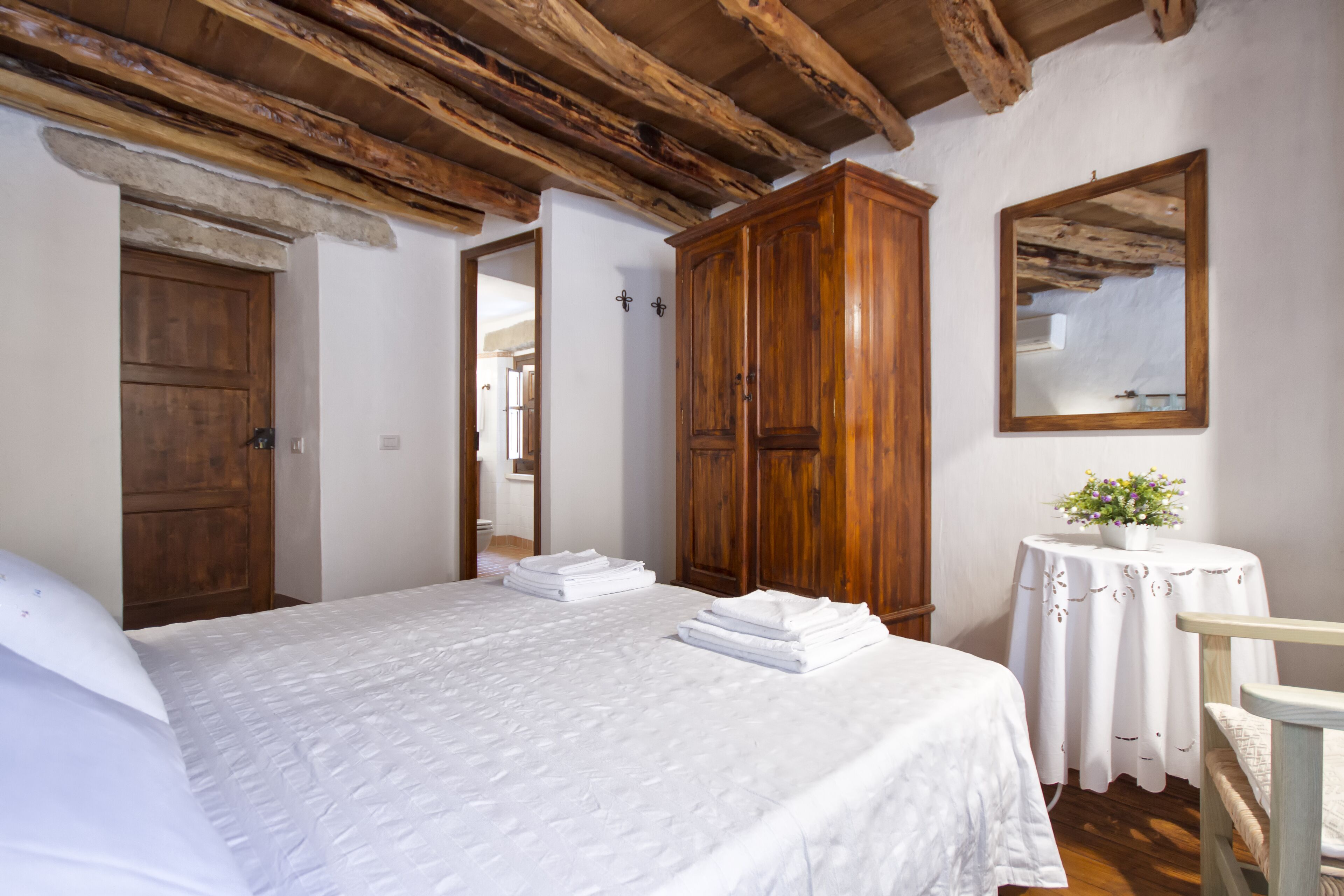 A bedroom with a large bed, wooden wardrobe, and a small table with a plant.